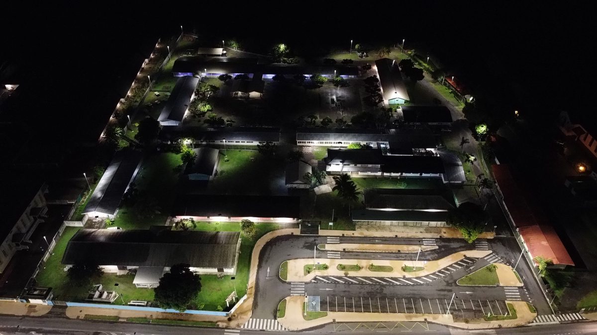 Le collège de Papara vu du ciel, de nuit : les préaux éclairés, les cours désertes et le parking devant la route de ceinture.
